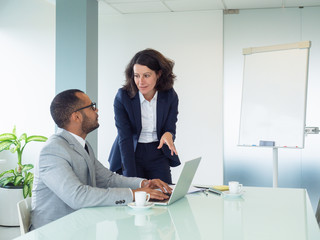 Senior female employee teaching male intern how to use corporate software. Business man sitting at...