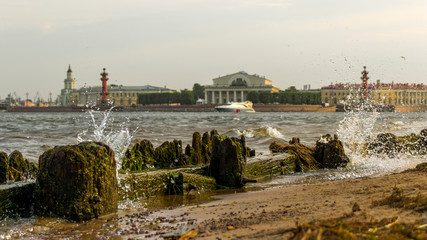 Fototapeta premium Saint Petersburg, Russia. View of the Spit of Vasilyevsky Island. The beach of the Peter and Paul Fortress. Neva River. Splashing waves breaking on the shore. Boat sailing on the Neva River.