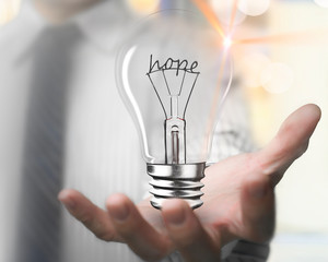 Businessman hand holding light bulb with hope word wire shape, front view, blur background.
