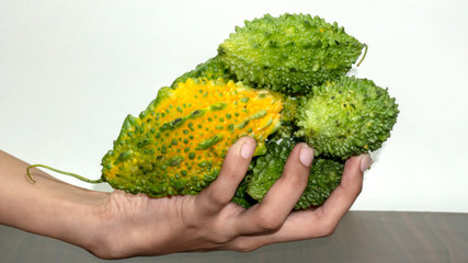 Many green and yellow bitter gourd in hand with wood chopping board isolated