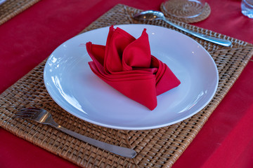 Elegant table setting with fork, spoon, white plate and red napkin in restaurant . Nice dining table set with arranged silverware and napkins