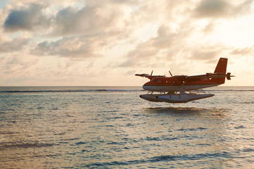 Summer sunset with seaplane. Landing seaplane on the dawn seashore. Calm scenery on evening sea.