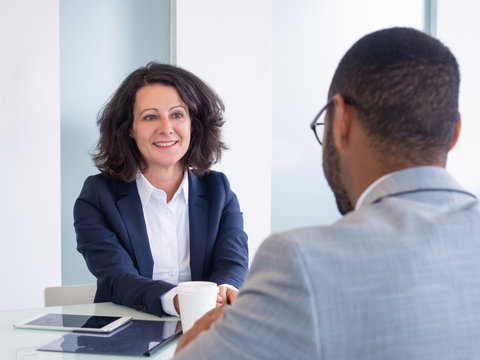 Smiling female job candidate talking to employer during interview. Business man and woman sitting at meeting table and talking. Career concept