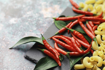 Uncooked pasta on a stone background. With seasonings and spices, spicy chili peppers.