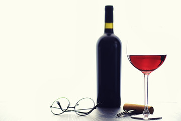 A glass of red dry wine on the table. Dark bottle and glass of wine.