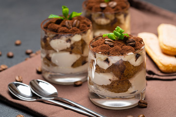 Classic tiramisu dessert in a glass cup on brown kitchen towel or napkin on dark concrete background