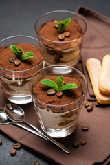 Classic tiramisu dessert in a glass cup on brown kitchen towel or napkin on dark concrete background