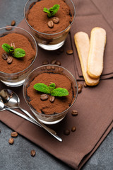 Classic tiramisu dessert in a glass cup on brown kitchen towel or napkin on dark concrete background