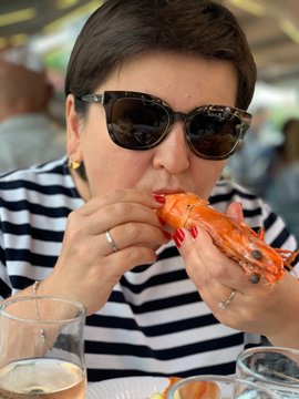 Woman in stripes is eating huge langustine in food court of seafood market in Trouville, Normandie