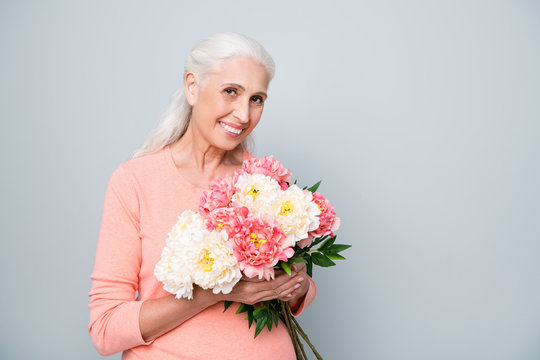 Close up photo of attractive charming gorgeous middle-aged granny holding big bouquet of white and pink peony in hand isolated grey background