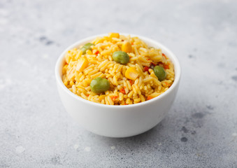 White bowl with boiled organic basmati vegetable rice on light stone background. Yellow corn and green peas with paprika slices. Top view