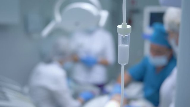 modern dental clinic during surgery, group of doctors treat patient under anesthesia room, an intravenous dropper with medicine into focus