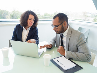 Female mentor teaching male intern how to use corporate software. Business colleagues sitting at...