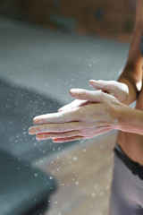 Woman climber is chalking and clapping hands with white chalk powder before climb in indoor climbing gym. woman getting ready to climbing. exercising and training in climbing gym. Close up view.