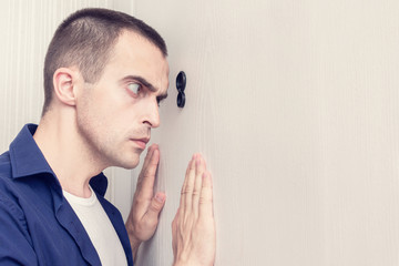 Handsome man look out through the peephole of front door, portrait, close up, toned