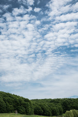 Obraz premium Clouds in the sky are like waves on the sea. Blue cloudy sky over green forest in summer season