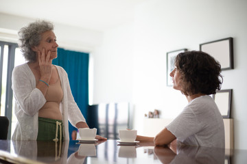 Fototapeta premium Serious mother and daughter talking at home. Side view of senior mother and middle aged daughter spending time together and looking at each other. Family concept
