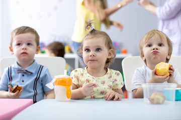 Nursery babies have a dinner in kindergarten. Little toddlers boys and girls sitting at the table...