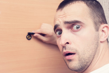 Scared man at the front door, peephole of front door, portrait, closeup, toned