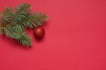 Christmas red ball and evergreen branch on red background with space for text. View from above. New Year card.