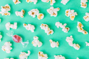 Closeup popcorn and red caramel dragee on a green background. Unhealthy diet concept. Minimalism, flat lay, top view, place for text.