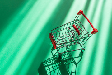 Small copy of a shopping cart for supermarkets on a green background. The concept of shopping,...