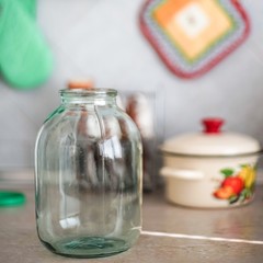 Empty three-liter jar is on the tabletop against the background of the pot and oven mitts.