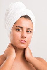 Portrait of a beautiful young woman in a bathroom. Youthful girl with perfect skin using facial cosmetics. White towel around the head..Skin care and health concept.