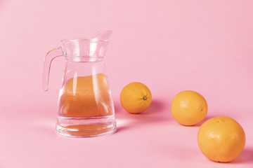 Oranges and jug of water on pink background