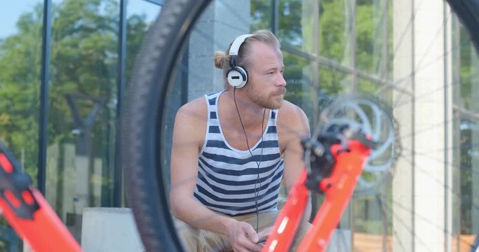 Young handsome male with colorful bicycle and headphones listen to music and ride by the summer streets, 4k futage 