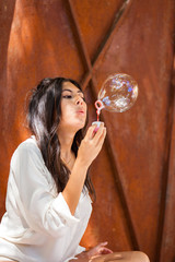 Beautiful young woman with white blouse blowing soap bubble..