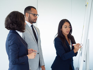 Young female analyst presenting marketing report to colleagues. Business woman drawing on board, her two coworkers looking at drawing. Flipboard concept