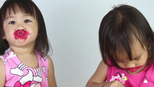Happy Asian child girl with her sister apply red lipstick on lips and make kiss to camera.