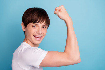Photo of cheerful funny positive boy pushing his arm muscles while isolated with blue background