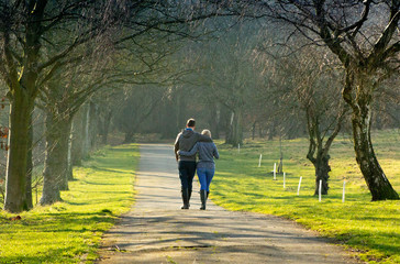 A young couple walking arm in arm through a park in the Spring sunshine