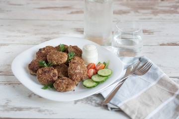 Juicy delicious meat cutlets in a white plate on a light wooden table.