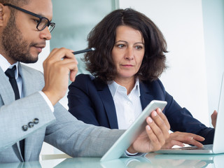 Business colleagues analyzing digital reports on tablet and laptop. Business man and woman sitting...