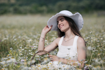 Beautiful girl outdoors with a bouquet of flowers in a field of white daisies,enjoying nature. Beautiful Model with long hair in white dress having fun on summer Field with blooming flowers,Sun Light.