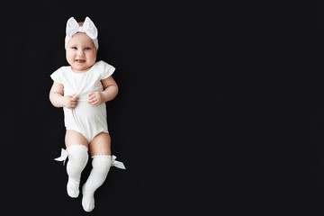 Cute cheerful baby girl wearing white clothes and headband on black background
