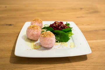 Salad with Beet and Sushi Balls on white Plate on wooden Table.