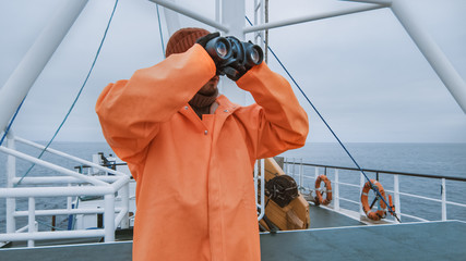 Captain of Commercial Fishing Ship Dressed in Protective Coat Looking through Binoculars