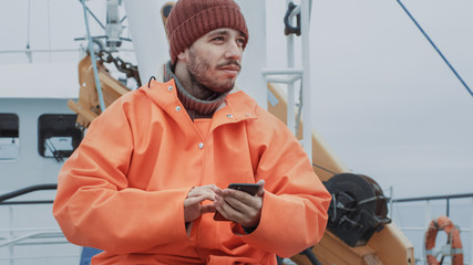 Casualy Dressed Fisherman Using Mobile Phone while Traveling on Ship.