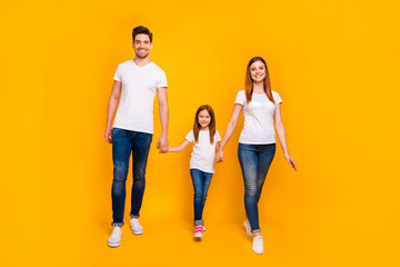 Naklejka premium Full length body size view of three nice attractive lovely stylish cheerful cheery friendly person holding hands spending weekend free time strolling isolated on bright vivid shine yellow background