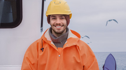 Portrait of Dressed in Bright Protective Coat Smiling Fisherman on Commercial Fishing Boat Looking...