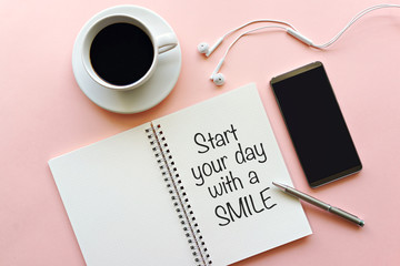 Start your day with a smile. Inspirational motivation quote on notebook with coffee, smartphone and earphone