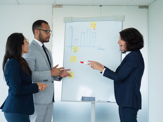 Successful trainer teaching new employee. Business woman standing at white board with marker and speaking her two colleagues looking at her. Teaching concept