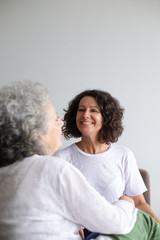 Happy mother and daughter spending time together. Cheerful middle aged woman sitting on couch and looking at elderly mother at home. Togetherness concept