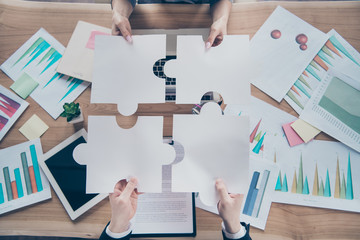 High angle view photo of four hands putting difficult puzzle pieces together above workshop table
