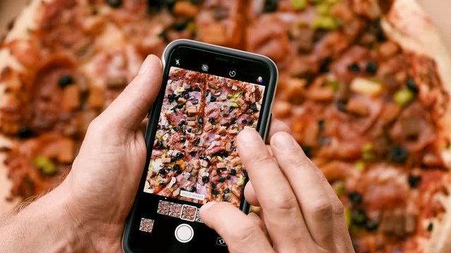 Male hands taking photo of delicious Italian pizza on smartphone. Man in restaurant make photo of food on mobile phone camera. Top view close-up. People and food concept.