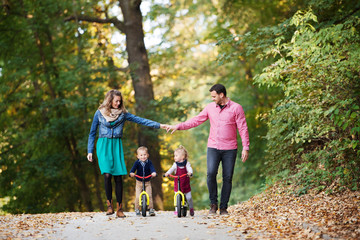 Beautiful young family with small twins on a walk in autumn forest.